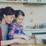 Smiling mother and cute daughter making Christmas cookies together sitting at modern kitchen at home. Family, food and people concept