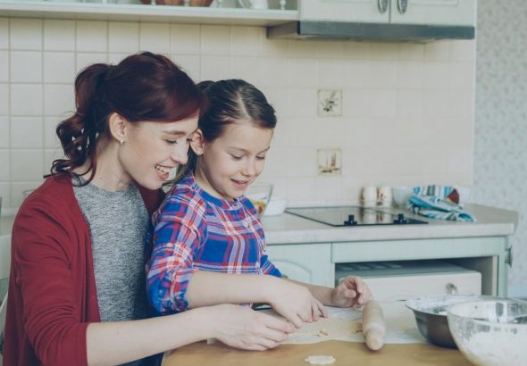 Smiling mother and cute daughter making Christmas cookies together sitting at modern kitchen at home. Family, food and people concept
